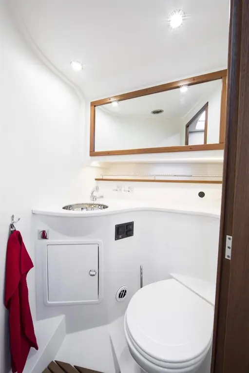 Compact bathroom with white walls, a mirror, a sink, and a toilet, featuring a red towel and various fittings.